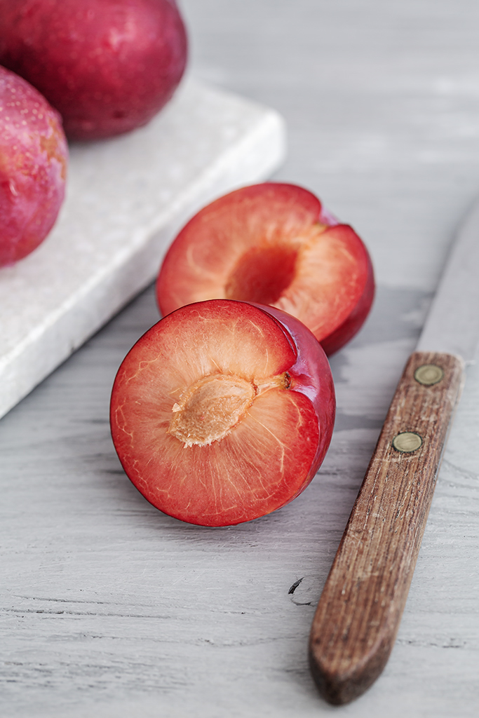 Zerteilte Pflaumen mit einem Messer auf einem hellen Holzuntergrund