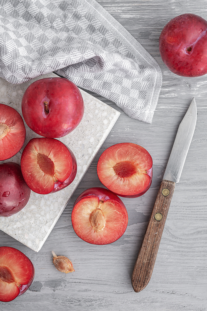 Zerteilte Pflaumen mit einem Messer auf einem hellen Holzuntergrund