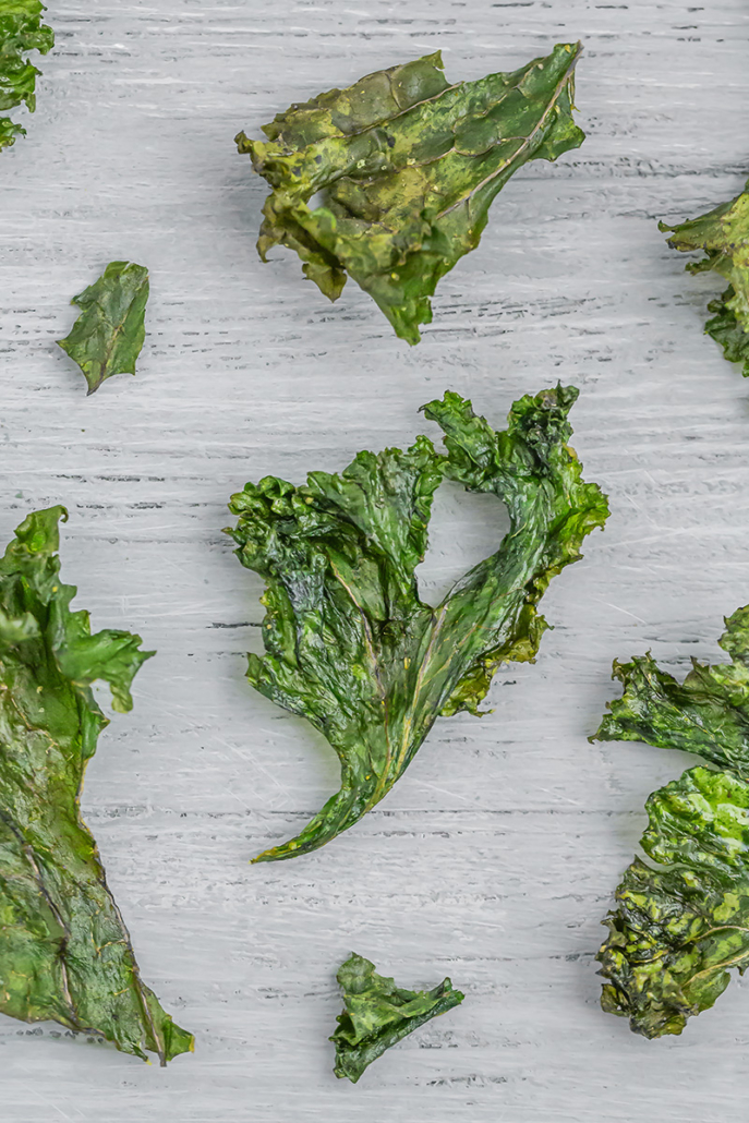 Einzelne Chips aus gebackene Grünkohl auf einem grauen Holzuntergrund