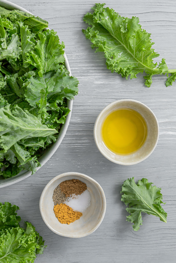 Frischer Grünkohl, Gewürze und Olivenöl auf einem hellen Holzuntergrund