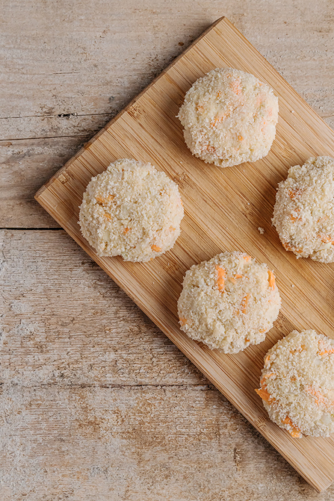Zum Braten vorbereitete Bratlinge aus Kohlrabi, Karotten und Hirse auf einem Holzbrett