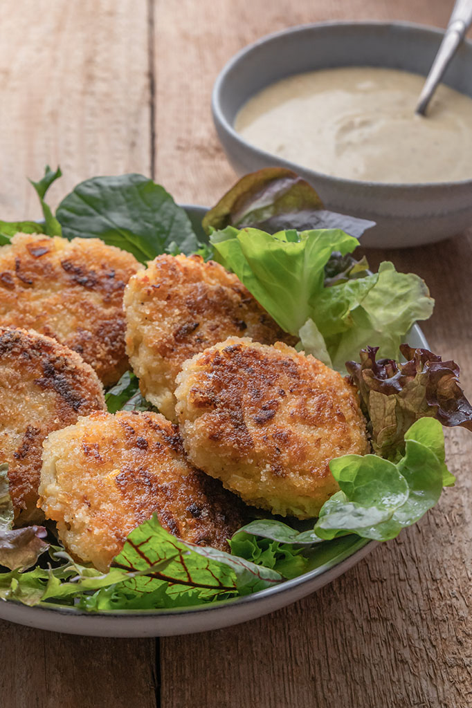 Fünf Kohlrabi-Karotten-Hirsetaler angerichtet auf Salat, daneben steht ein Curry-Dip.