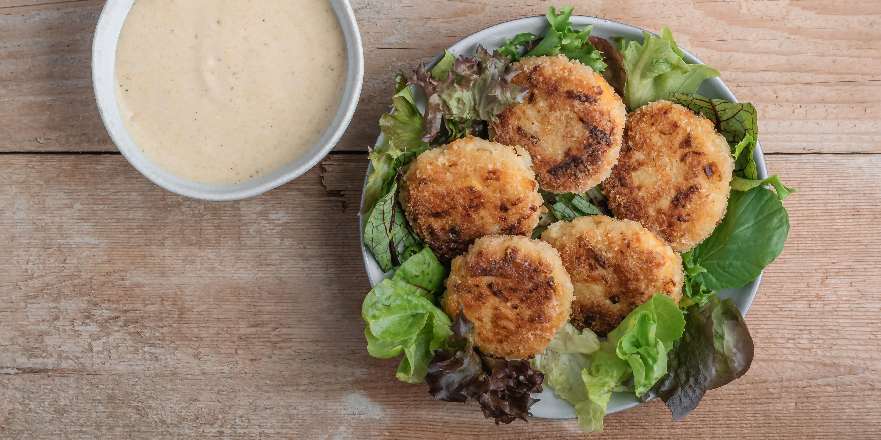 Fünf Kohlrabi-Karotten-Hirsetaler angerichtet auf Salat, daneben steht ein Curry-Dip.
