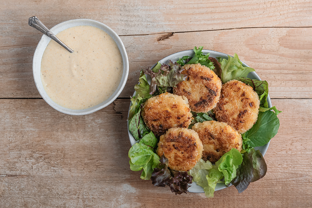 Fünf Kohlrabi-Karotten-Hirsetaler angerichtet auf Salat, daneben steht ein Curry-Dip.