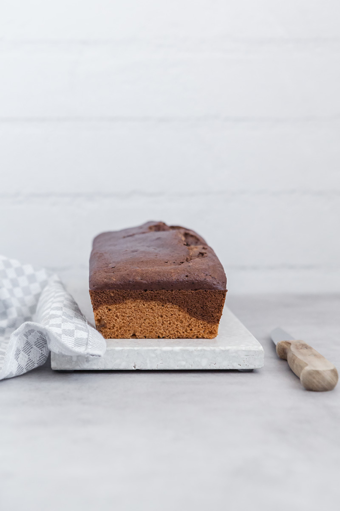 Frisch gebackener Marmorkuchen auf einem Scheidebrett, daneben liegt ein Messer.