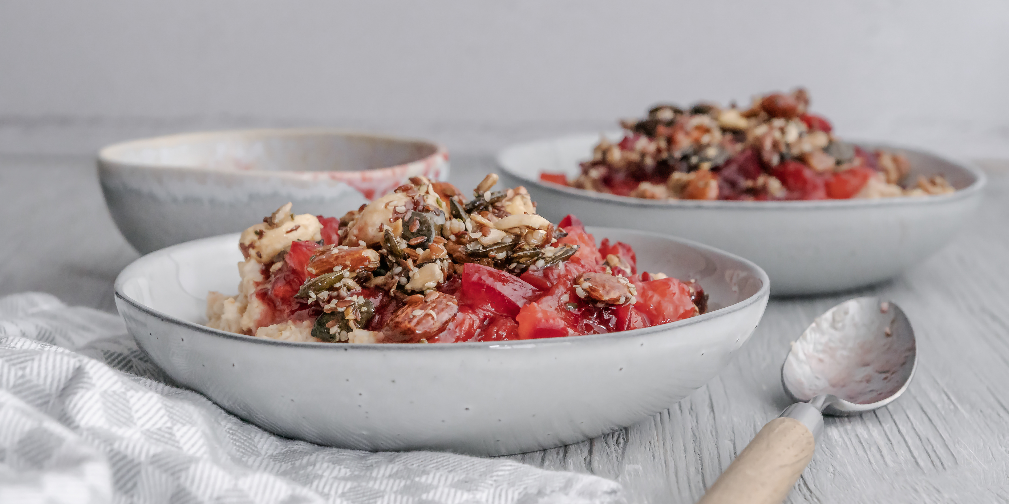 Warmes Frühstück aus Porridge, Pflaumenkompott und Nüssen mit einem Hauch Zimt