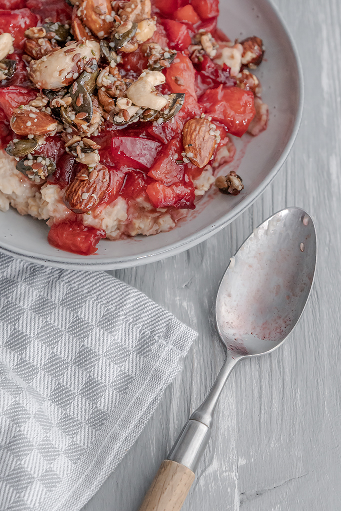 Warmes Frühstück aus Porridge, Pflaumenkompott und Nüssen mit einem Hauch Zimt.