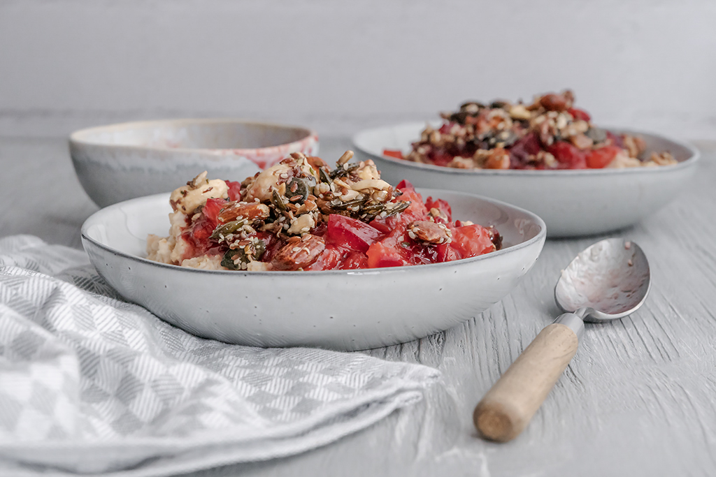 Warmes Frühstück aus Porridge, Pflaumenkompott und Nüssen mit einem Hauch Zimt.
