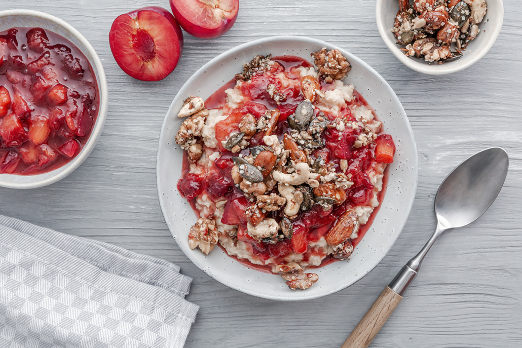 Warmes Frühstück aus Porridge, Pflaumenkompott und Nüssen mit einem Hauch Zimt.