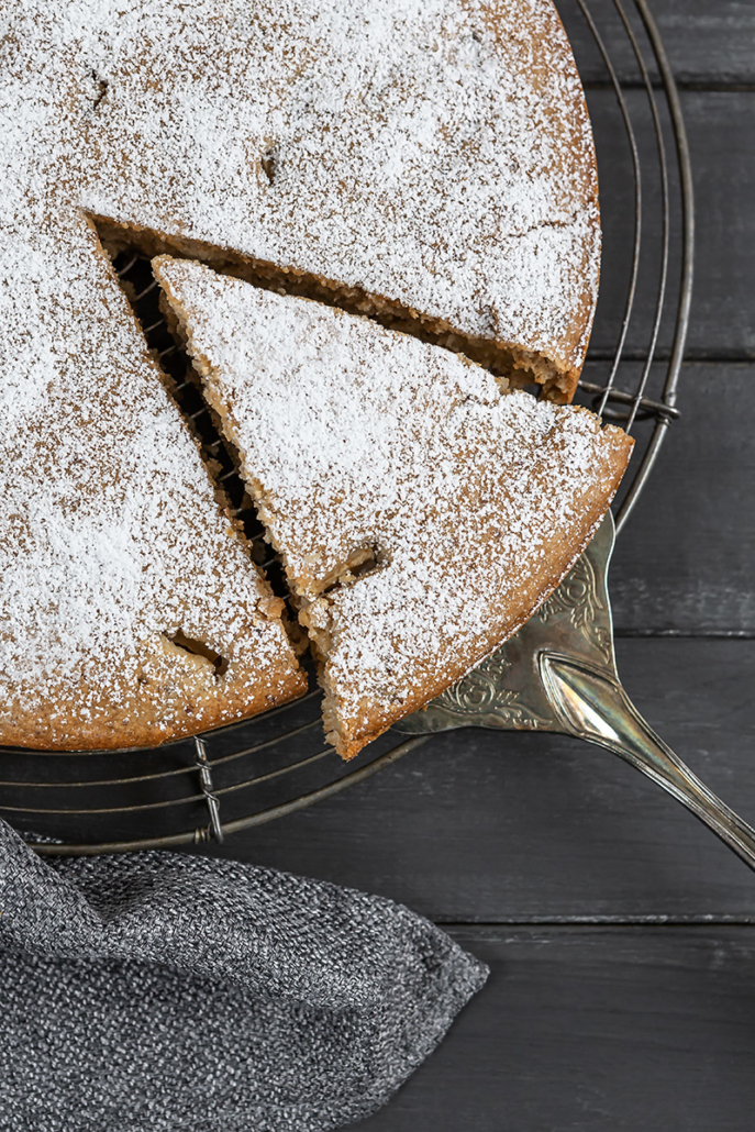 Angeschnittener Rührkuchen mit Äpfeln und Zimt auf einem Kuchengitter. Ein Stück wird mit dem Kuchenheber herausgezogen.