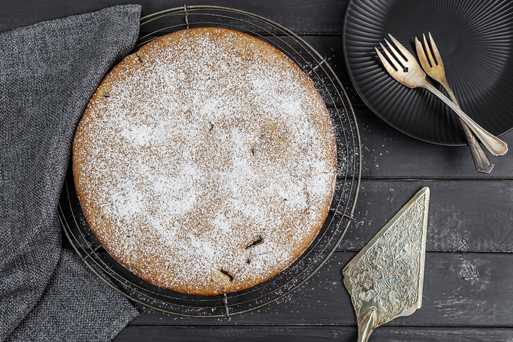Rührkuchen mit Äpfeln und Zimt auf einem Kuchengitter. Daneben liegt ein Kuchenheber und ein Teller mit zwei Kuchengabeln steht bereit.