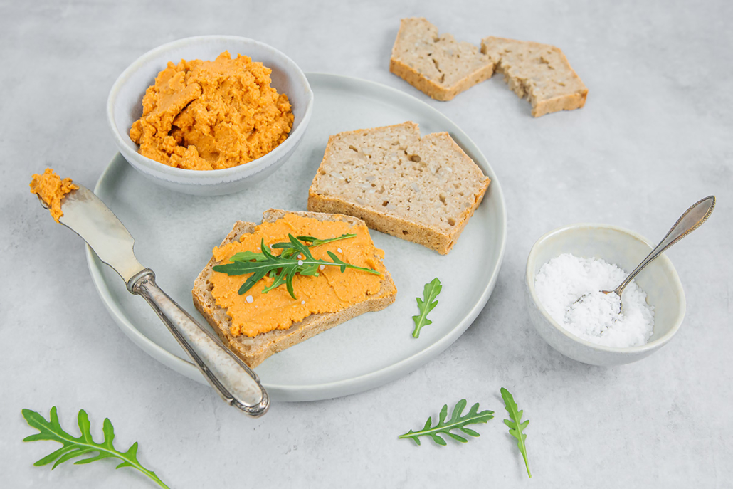 Teller mit zwei Scheiben Brot und einem Schälchen Linsenaufstrich, eine Scheibe Brot ist mit Aufstrich bestrichen