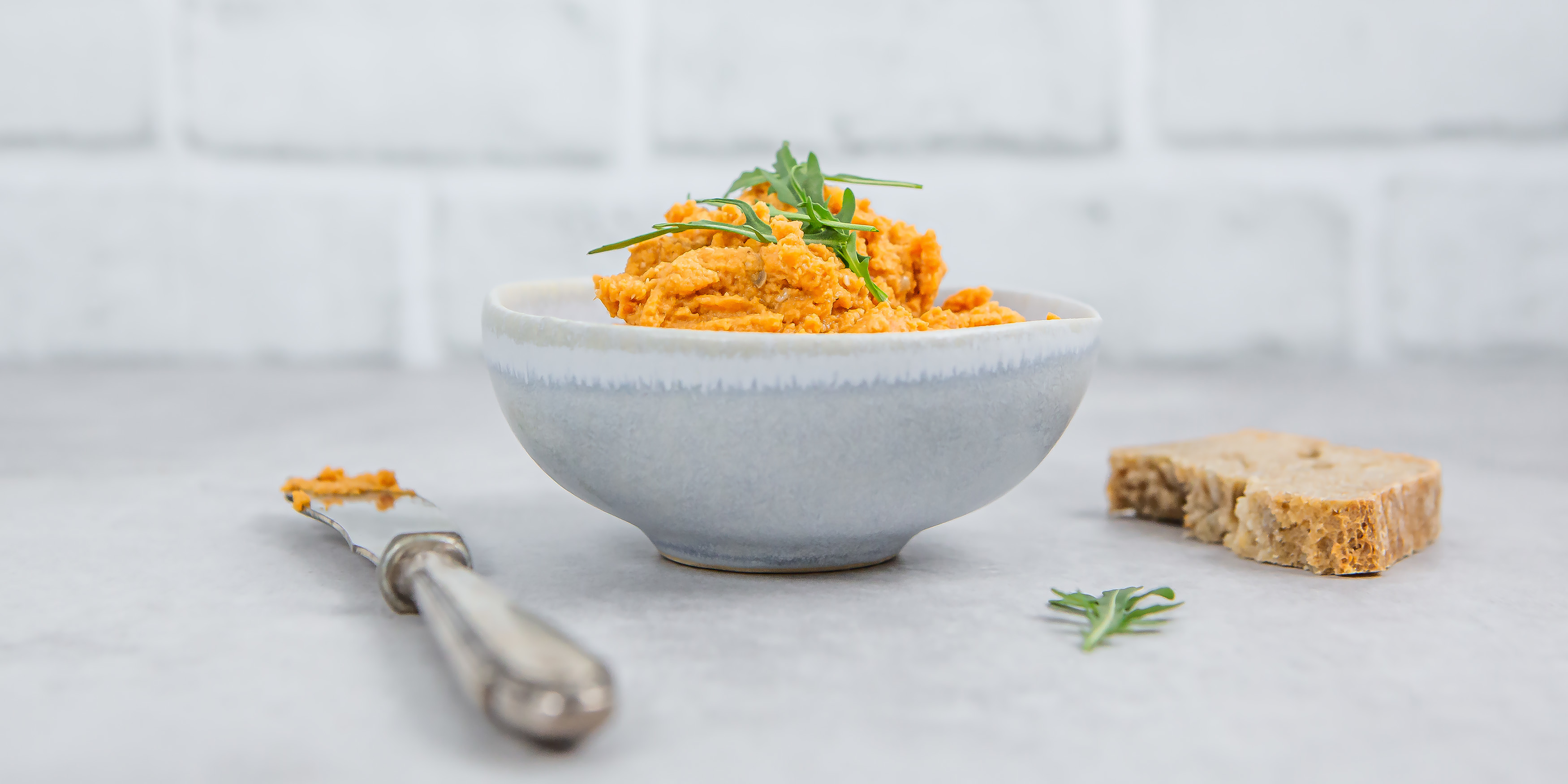 Linsenaufstrich aus roten Linsen und Harissa in einer kleinen Schüssel, daneben liegt ein Messer