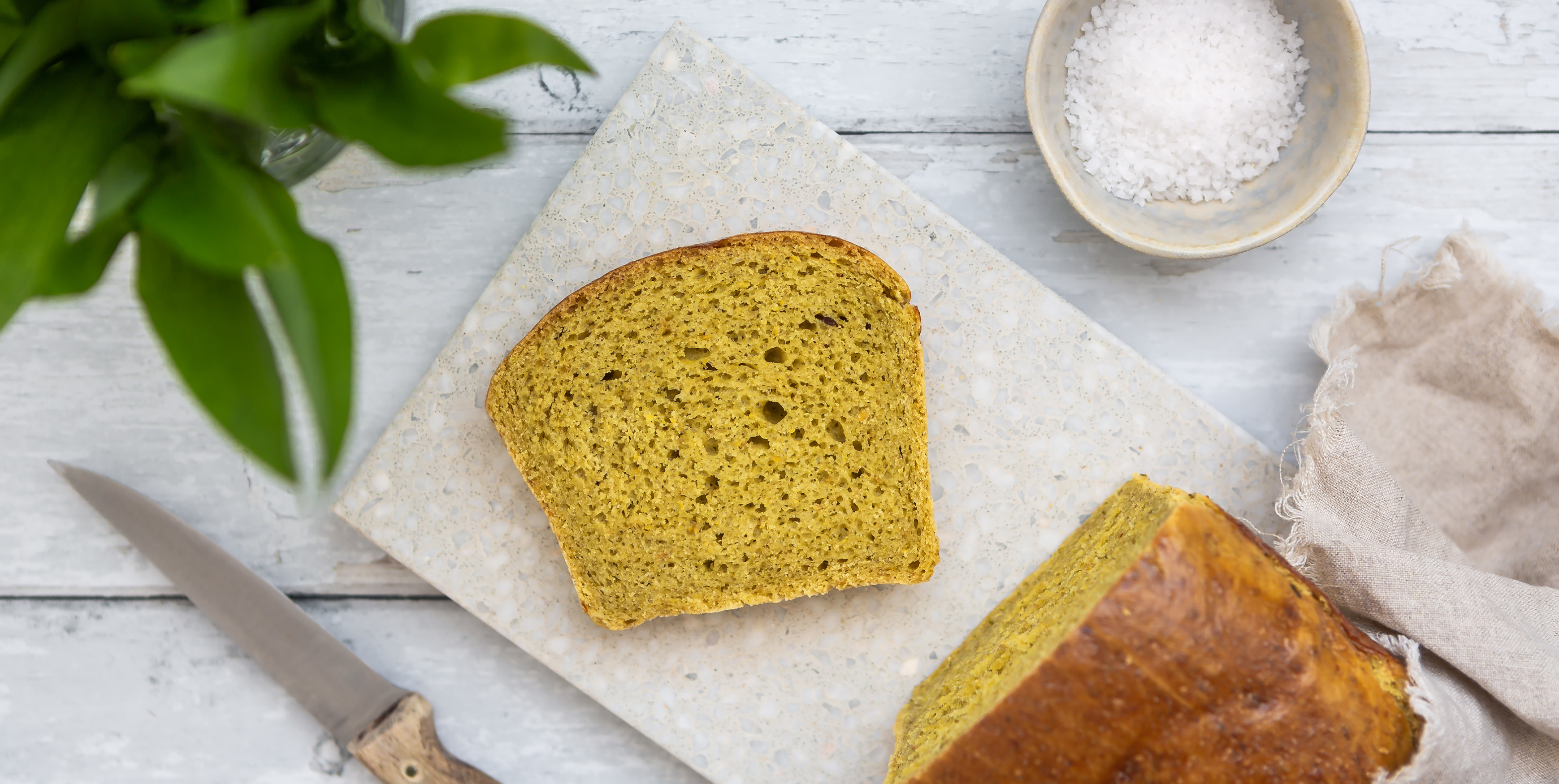 Angeschnittener Laib Bärlauch-Brioche auf einem Schneidebrett, daneben steht ein Glas mit frischem Bärlauch.