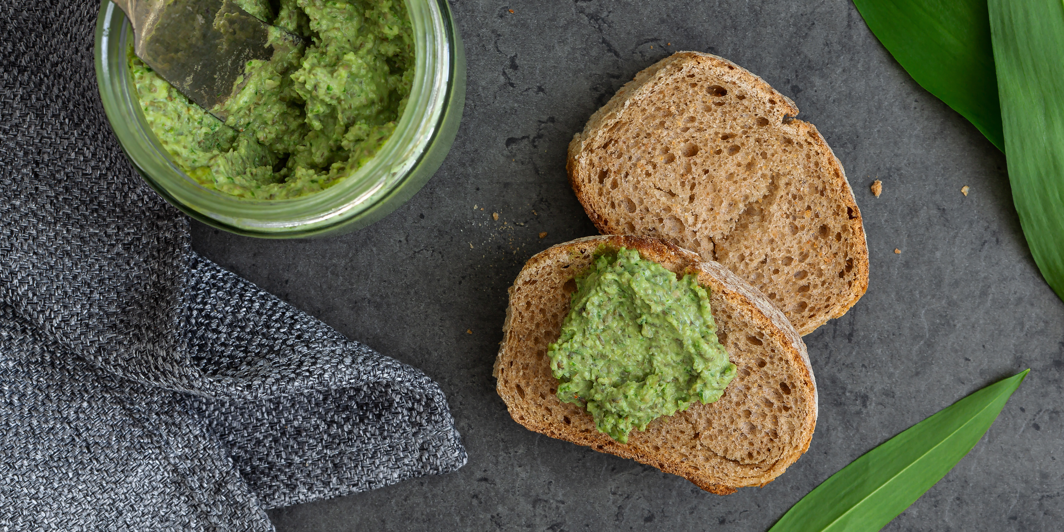 Brot mit Bärlauch-Linsen-Aufstrich, daneben steht das Glas mit dem Aufstrich und einem Messer.